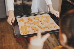 Cute little daughter and mother holding tray with christmas cookies close up in modern kitchen. Cute toddler girl and mom baking gingerbread cookies. Family holiday preparation, xmas culinary