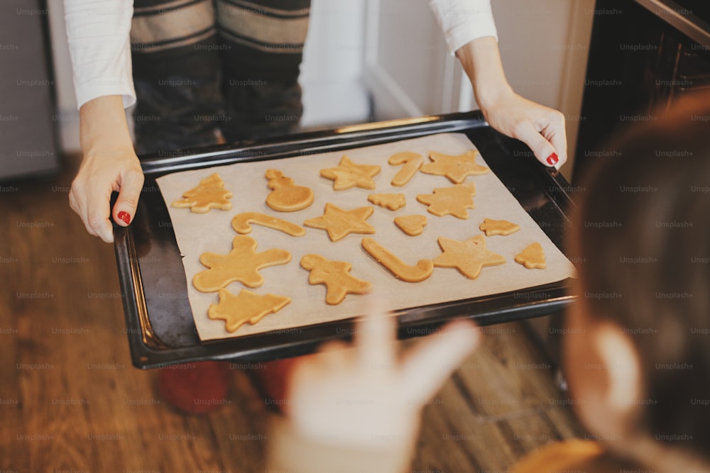 Jolie petite fille et mère tenant un plateau avec des biscuits de Noël en gros plan dans une cuisine moderne. Jolie petite fille et maman faisant des biscuits en pain d’épice. Préparation des vacances en famille, Noël culinaire