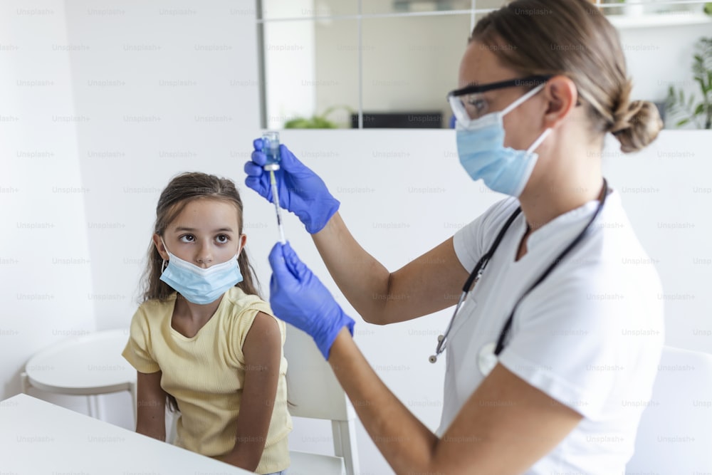 Concepto de campaña de inmunización antiviral. Médico vacunando a la niña. Niña con máscaras médicas vacunándose contra el covid-19, médico inyectando la vacuna contra el coronavirus en el hospital.