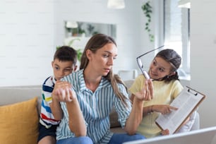 Young mother working with laptop while her son and daughter are playing in the living room. Mother trying to work from home