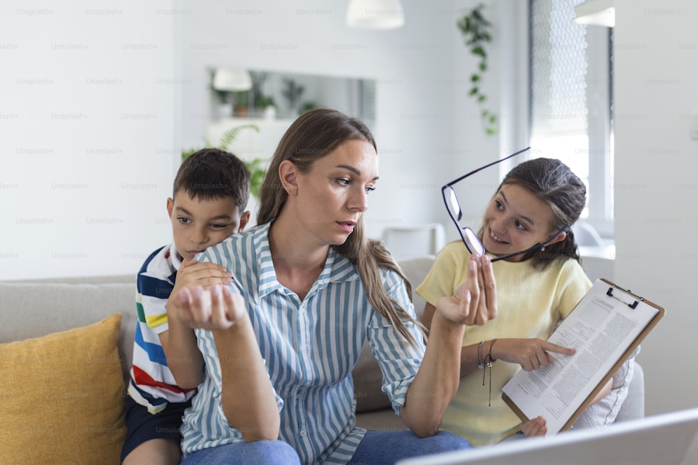 Young mother working with laptop while her son and daughter are playing in the living room. Mother trying to work from home