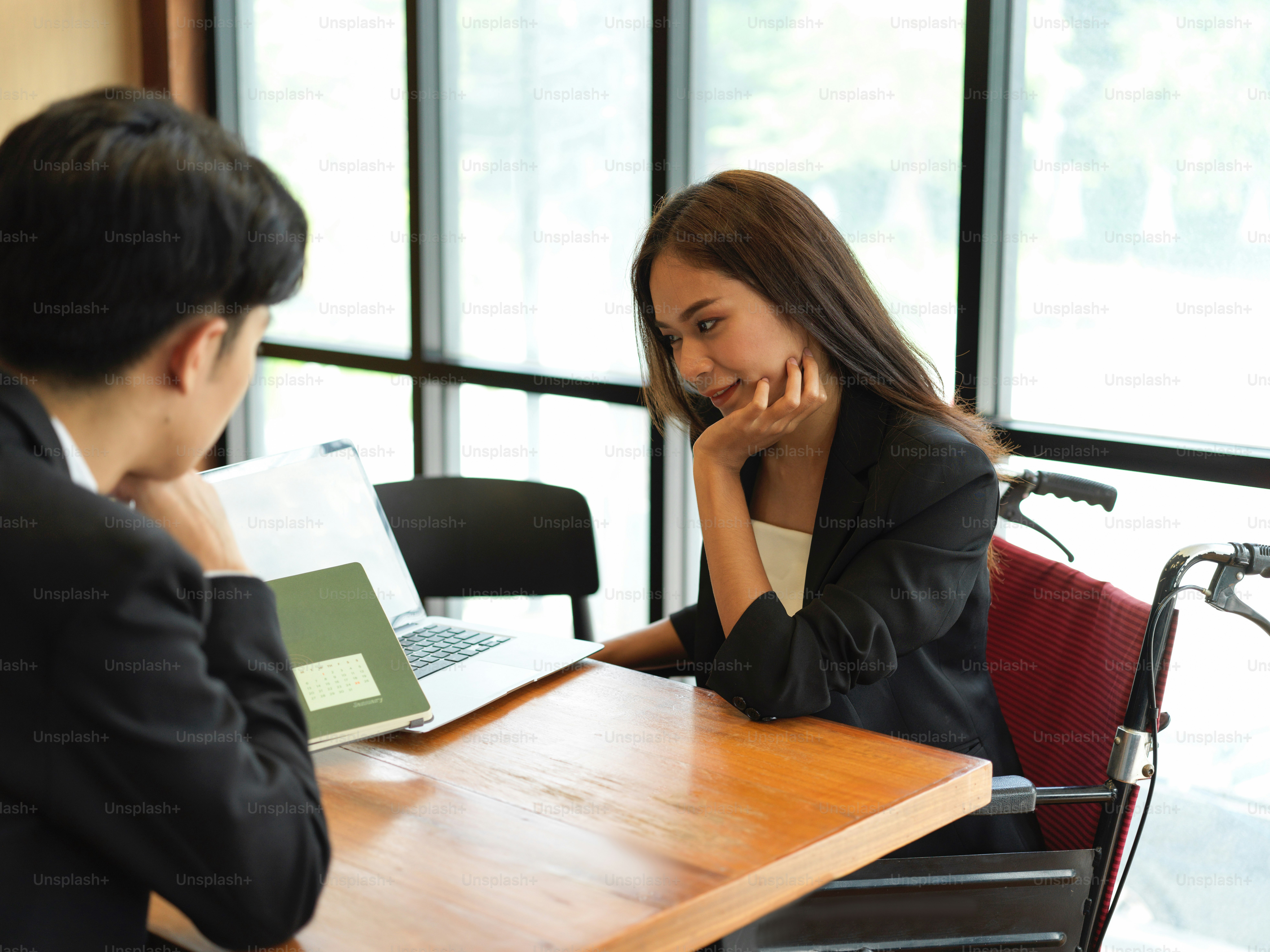 Friendly businessman having a good conversation with female employee in wheelchair. Businesswoman in wheelchair listening her partner explain work task