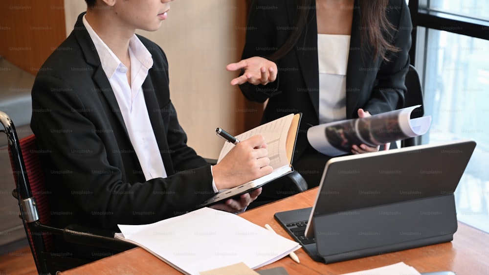 Young office disabled male worker in wheelchair working with his colleague in office.