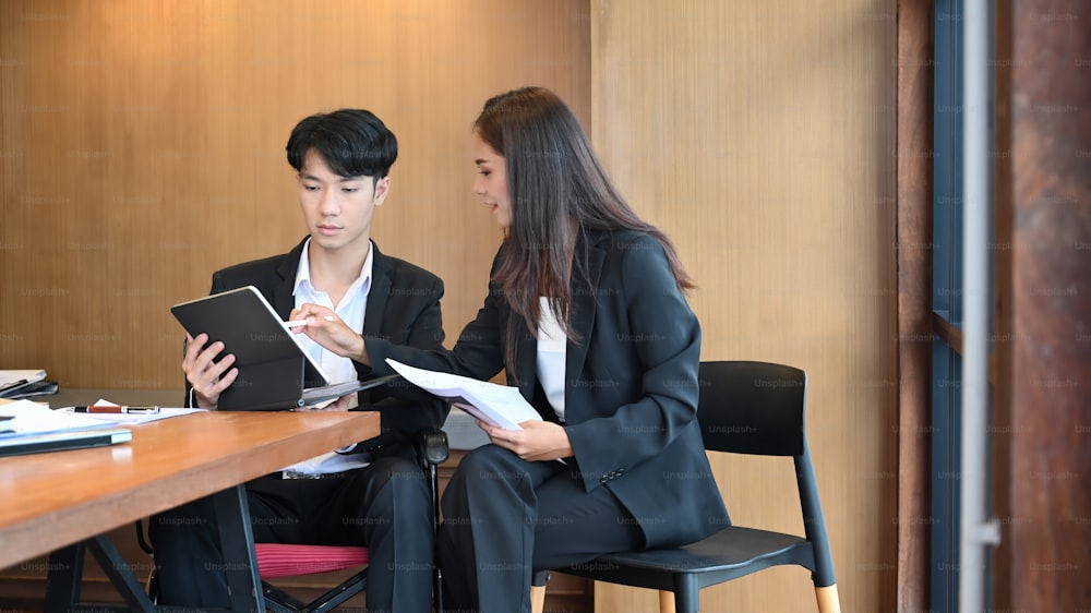 Young male office worker in a wheelchair sitting in office and working with his colleague.