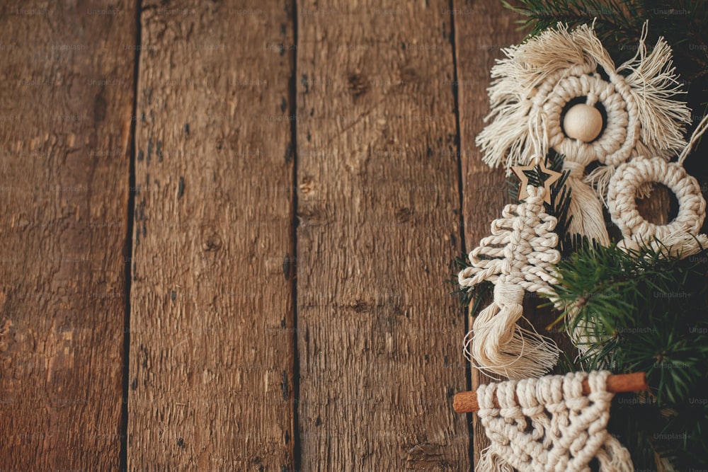 Des ornements élégants en macramé d’arbre de Noël et des branches de sapin bordent sur une pose plate en bois rustique. Ornements boho fait à la main pour les vacances de Noël. Décor scandinave, jouets écologiques. Espace pour le texte