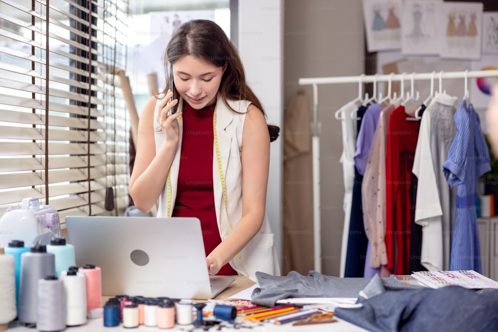 Millennial woman dressmaker making a phone call to her partner while holding her smartphone to her ear. A designer decorator speaks with a client about model features and color choices.