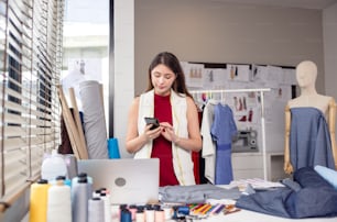 Millennial woman dressmaker making a phone call to her partner while holding her smartphone to her ear. A designer decorator speaks with a client about model features and color choices.