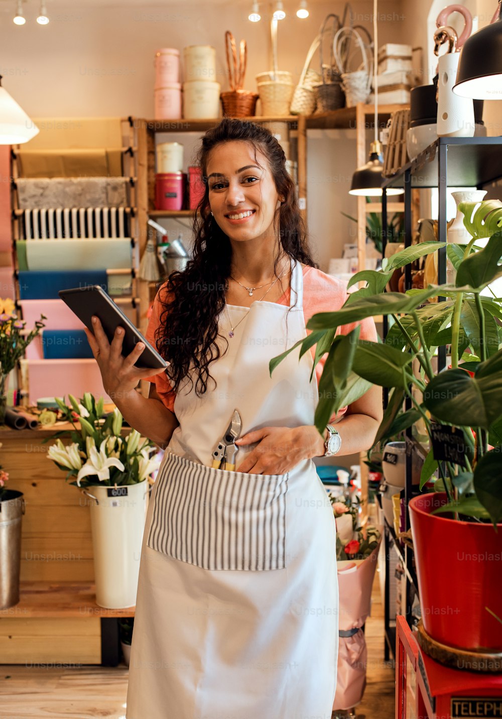 Young female florist with tablet working in her flower shop arranging houseplant.
