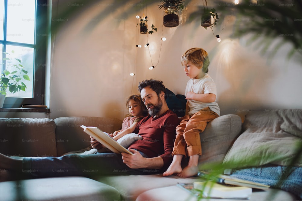Um pai maduro com dois filhos pequenos descansando dentro de casa, olhando para o álbum de fotos.