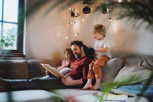 A mature father with two small children resting indoors at home, looking at photo album.