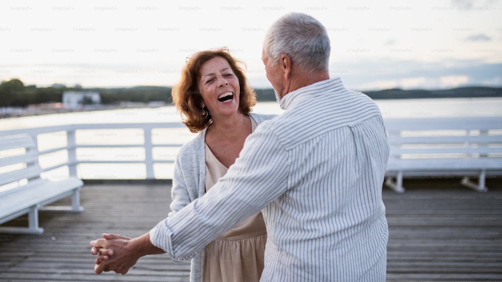Ein fröhliches älteres Paar, das draußen auf dem Pier am Meer tanzt und sich gegenseitig ansieht.