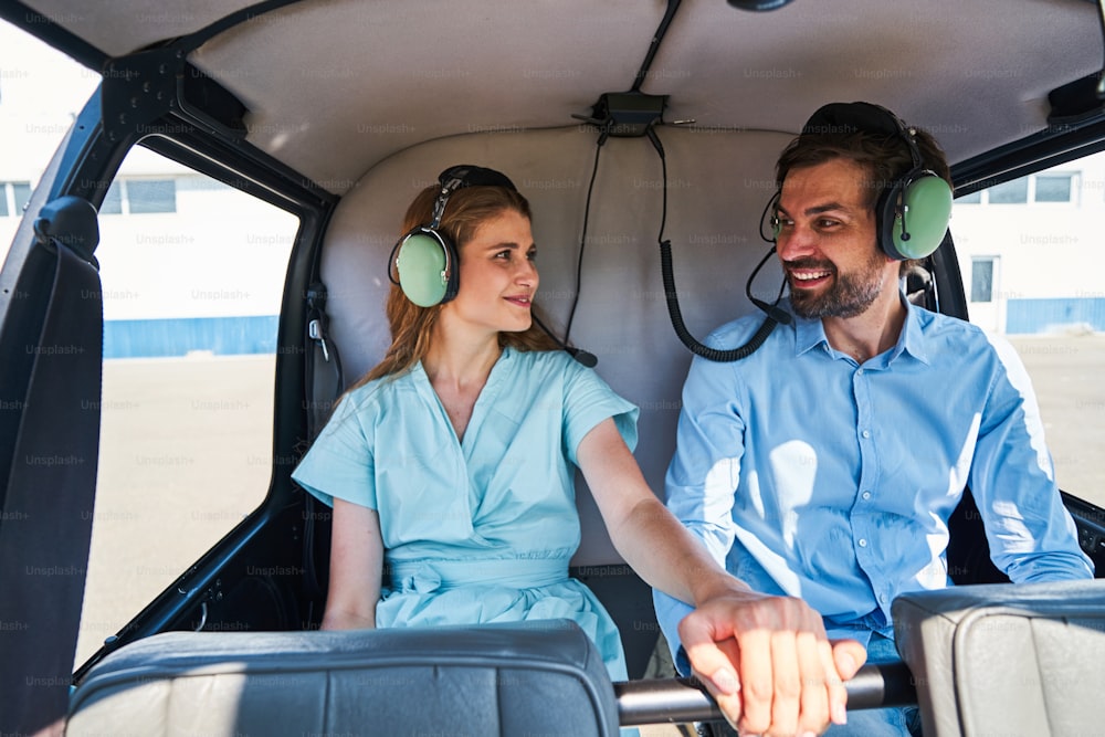 Smiling Caucasian woman and cheerful man sitting in backseats in helicopter cabin