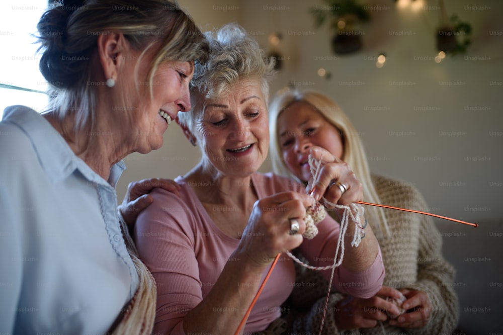 Amigas seniores felizes se divertindo tricotando juntas dentro de casa em casa.
