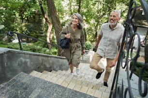 Complete relax. Low angle view of the happy mature couple resting on the nature. They walking up stairs and smiling. Retirement people concept