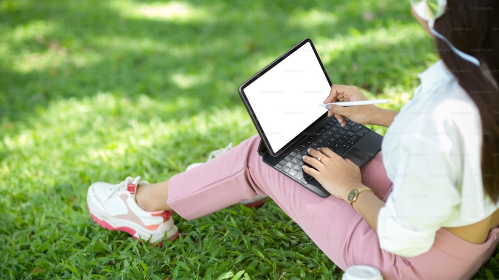 Lifestyles concept, Female sits in a beautiful park and working on digital tablet, typing work on tablet computer. tablet blank screen mockup