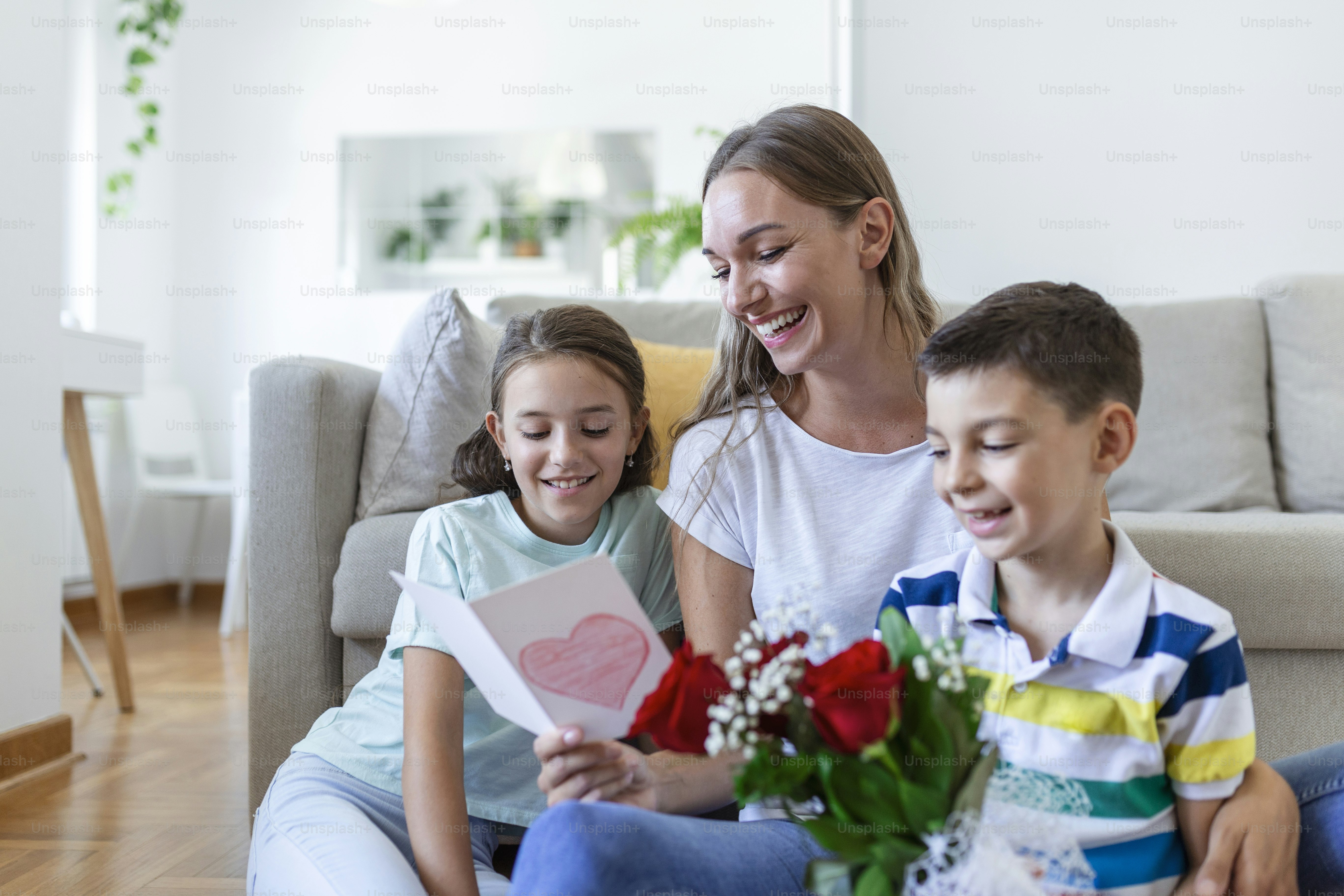 Fröhliche junge Mutter und kleine Kinder sitzen auf dem Sofa und ...