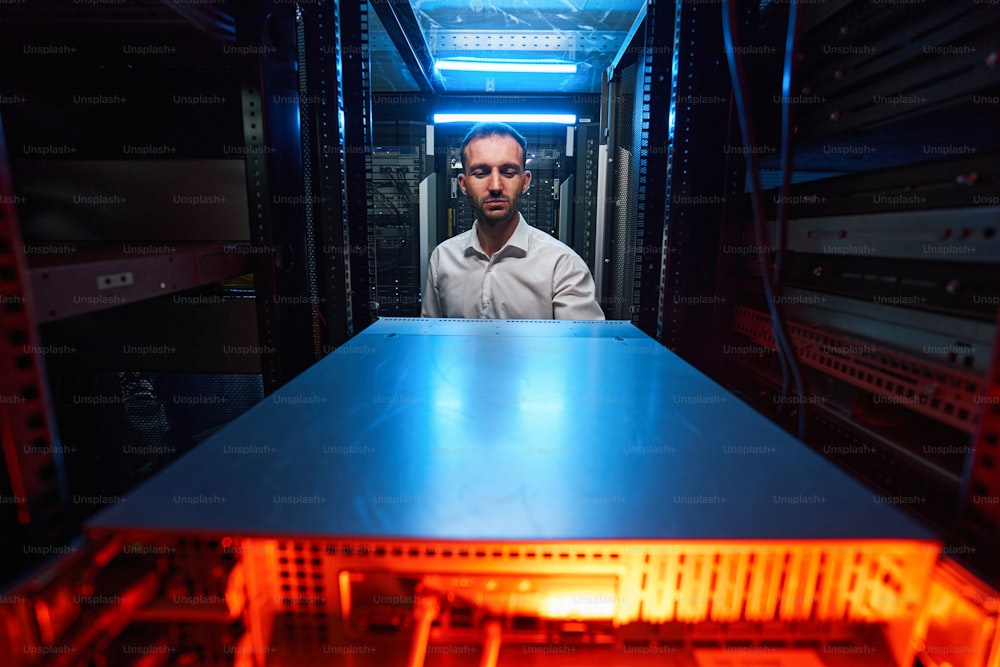 Front view of male server engineer configuring network cabinet in data storage facility