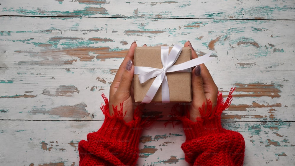 Above view woman in red sweater holding gift box on a wooden background.