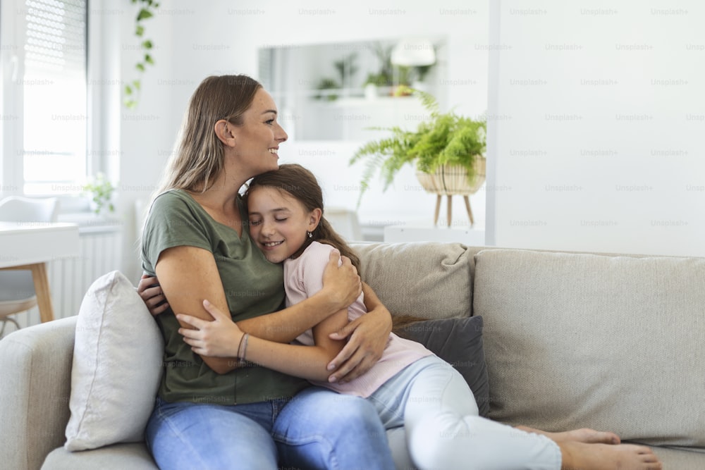 Close up of sweet pretty daughter cuddling with her young mother. Lovely mother embracing her cute daughter on the sofa at home.