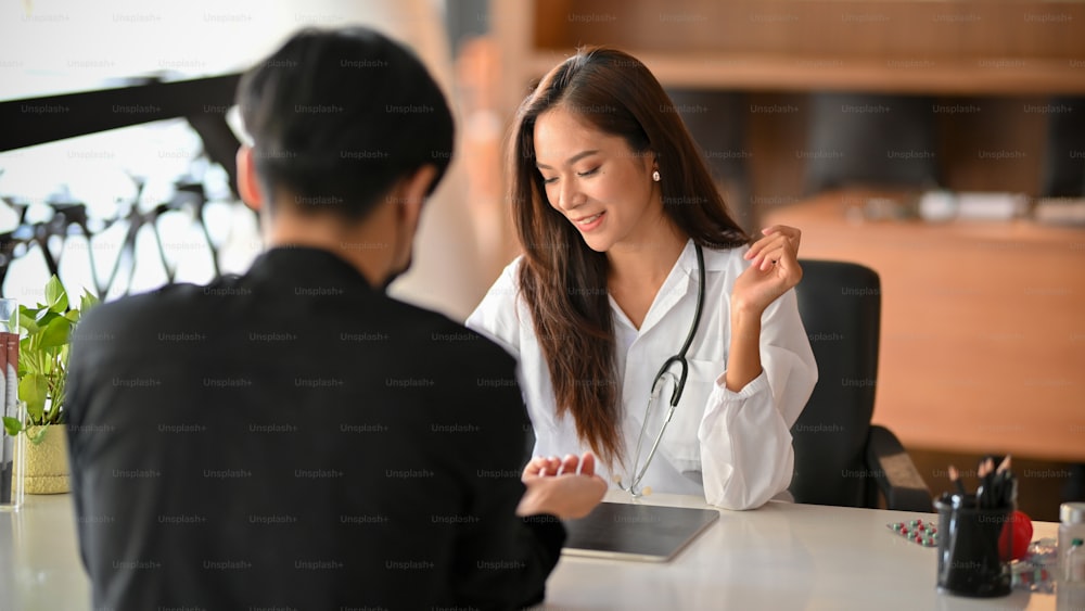 Cheerful asian female doctor discusses the medical treatment plan with male patient in examination room. Male patient make a follow-up appointment with a female physician.