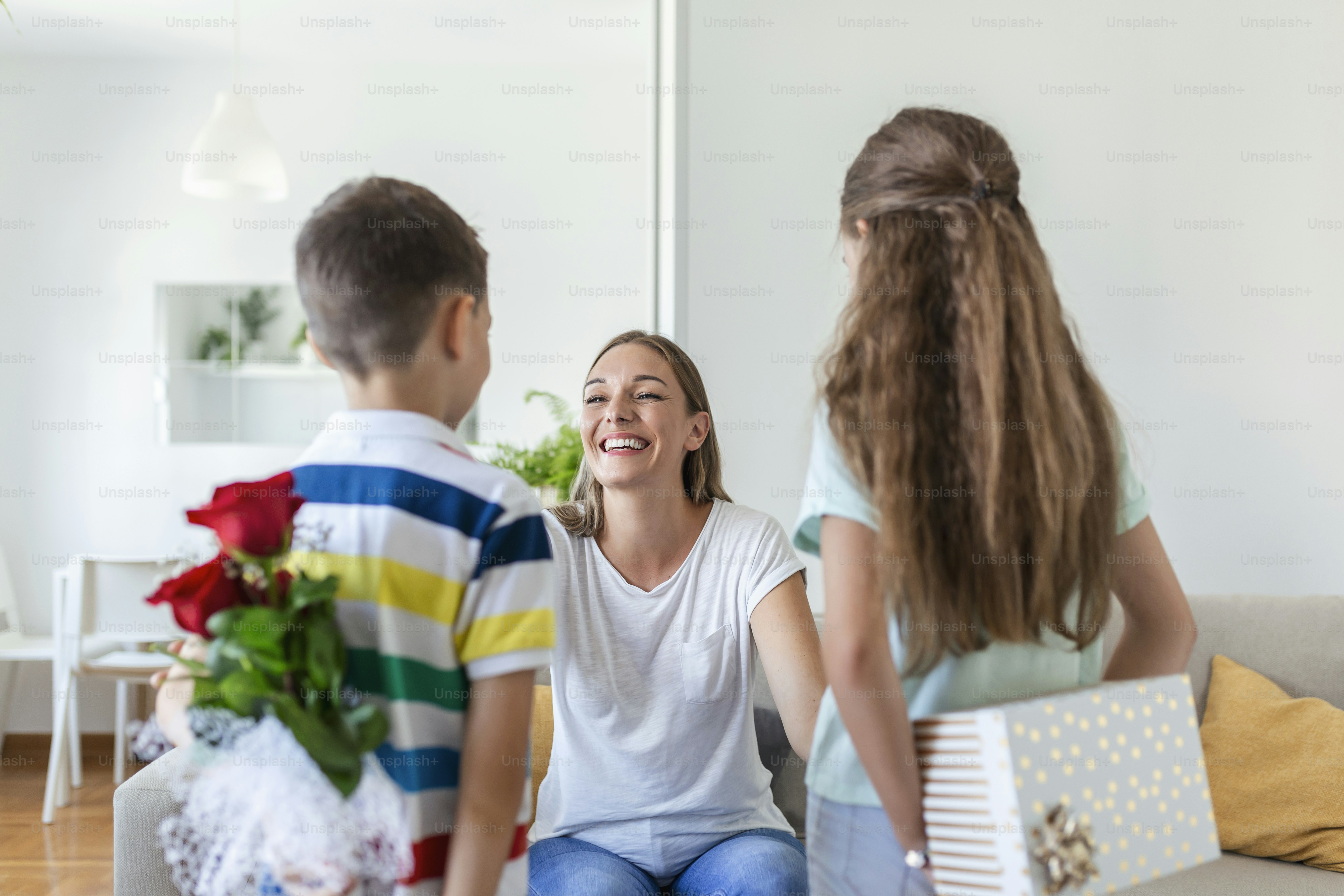 お母さんに花を贈る幸せな子供たち。母の日おめでとう!子供たちの男の子と女の子は笑顔の母親を祝福し、休日のお祝い中にバラの花束とギフトボックスを花に与えます