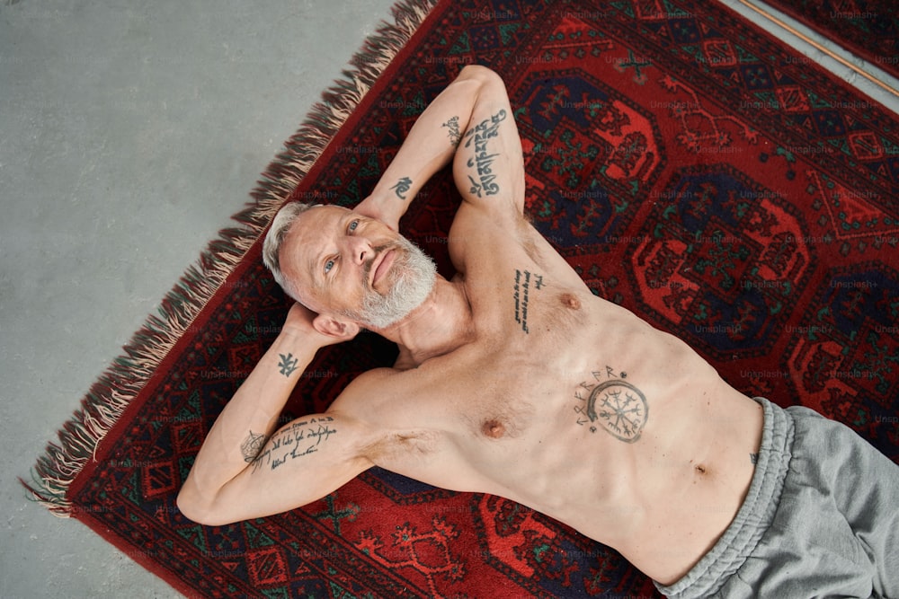 Entspannen. Hochwinkelansicht des nackten Mannes mit Tattoos, der nach dem Training auf dem Boden liegt und sich entspannt, während er über etwas nachdenkt. Archivfoto