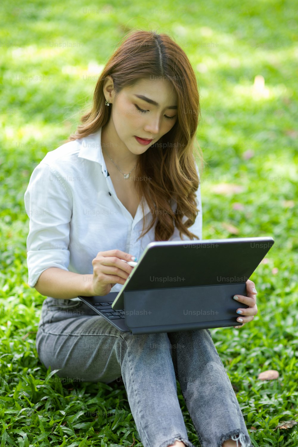 Charmante femme asiatique assise dans la cour à l’aide d’une tablette portable. Travailler à l’extérieur et se détendre