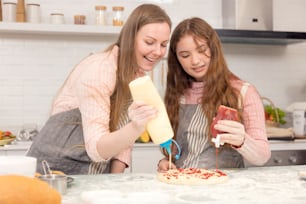 In the kitchen at home, a playful mother and daughter yell while making pizza dough.
