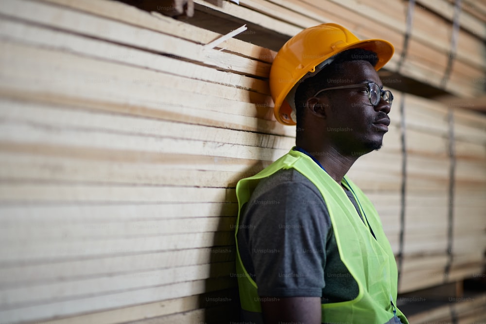 材木流通部門で働きながら何かを考えている若い黒人倉庫労働者。