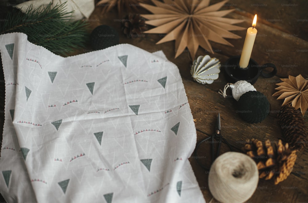 Furoshiki wrap. Modern fabric, scissors, craft paper star, candle, ornaments on rustic wooden table. Atmospheric moody time, nordic style. Zero waste and eco friendly presents. Merry Christmas!