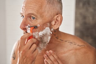 Casi listo. Retrato de un hombre mayor con el pelo gris afeitándose en su dormitorio. Chico barbudo deshaciéndose de la barba incipiente. Concepto de cuidado de la piel. Foto de archivo