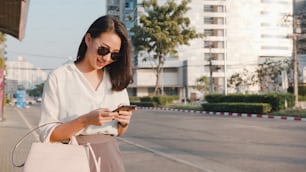 Successful young Asia businesswoman in fashion office clothes hailing on road catching taxi and holding smart phone while standing outdoors in urban modern city. Business on the go concept.