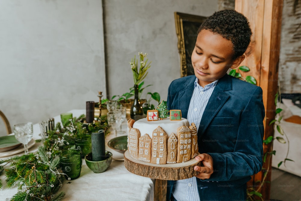 Boy holding Christmas cake decorated with handmade house gingerbreads. Idea for diy handmade Happy New Year festive sweets.