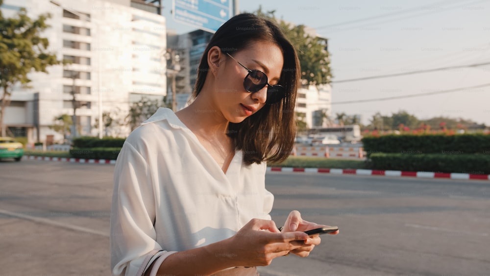 Successful young Asia businesswoman in fashion office clothes hailing on road catching taxi and holding smart phone while standing outdoors in urban modern city. Business on the go concept.