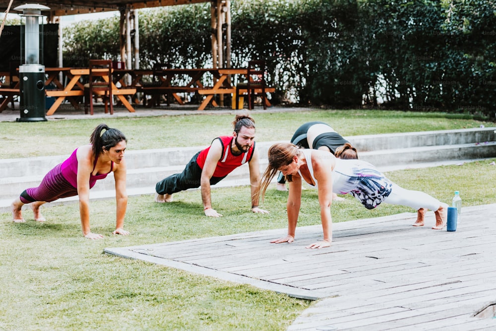 Groupe de jeunes hispaniques avec un entraîneur faisant des exercices de pompes dans le jardin en Amérique latine