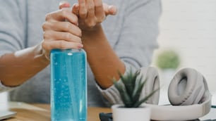 Asia lady using alcohol gel hand sanitizer wash hand before open tablet for protect coronavirus. Female push alcohol to clean for hygiene when social distancing stay at home and self quarantine time.