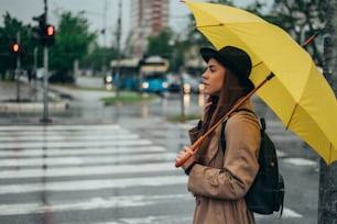 Hermosa joven que sostiene un paraguas amarillo mientras está en la ciudad mientras llueve