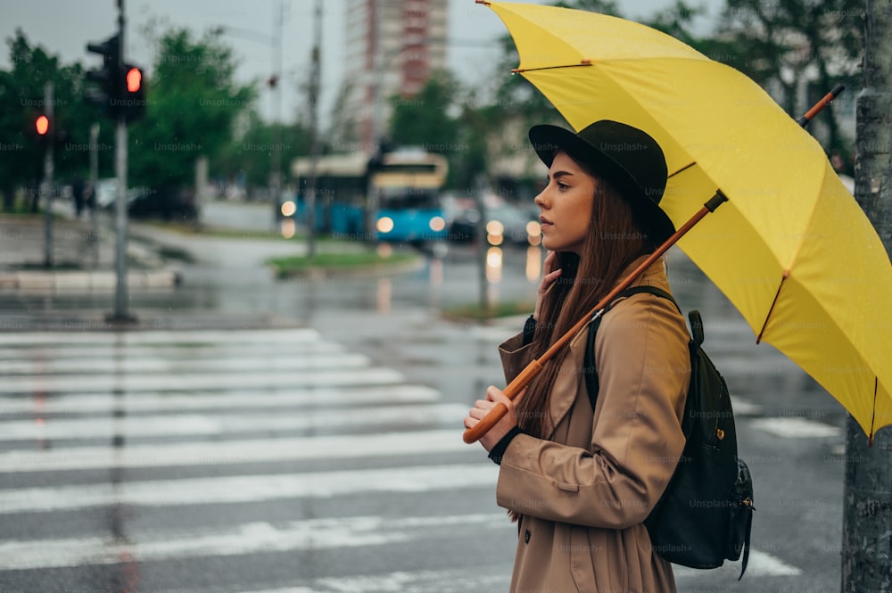 Beautiful young woman holding yellow umbrella while in the city while it rains