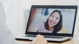 Young Asian business female using laptop video call talking with friends while working from home at bed room. Self-isolation, social distancing, quarantine for coronavirus in new normal concept.