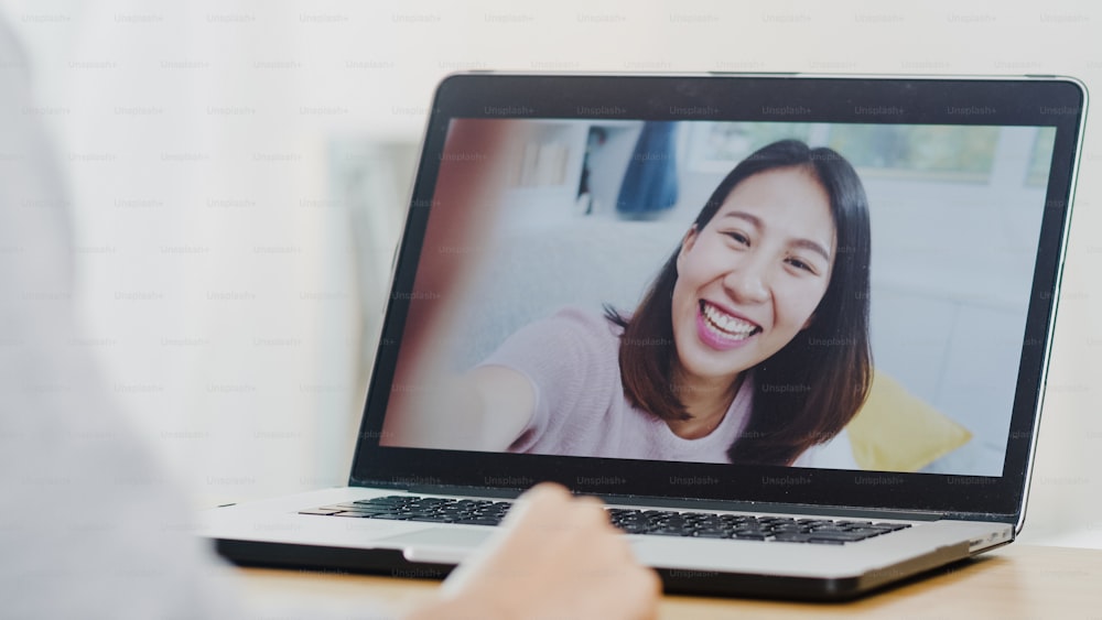 Young Asian business female using laptop video call talking with friends while working from home at bed room. Self-isolation, social distancing, quarantine for coronavirus in new normal concept.