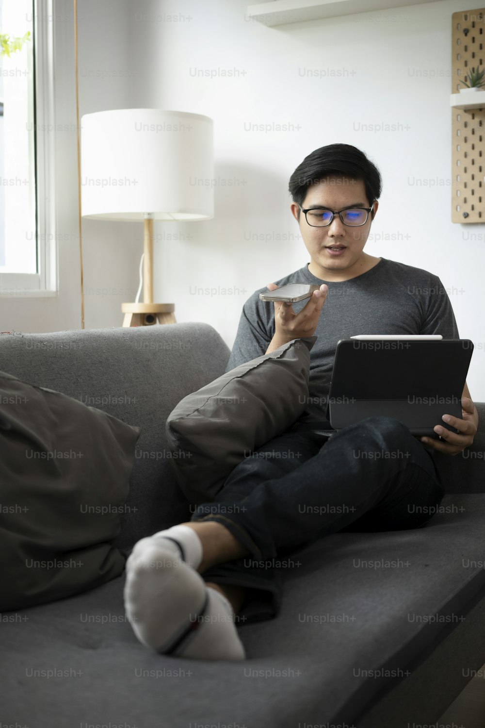 Young man working with computer tablet and talking on mobile phone in living room.