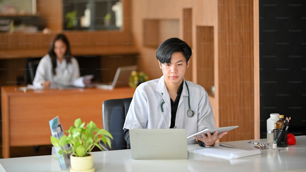 Un joven médico está usando una computadora portátil. En el consultorio del hospital, un médico lee un plan de cirugía y realiza una investigación médica en una computadora portátil