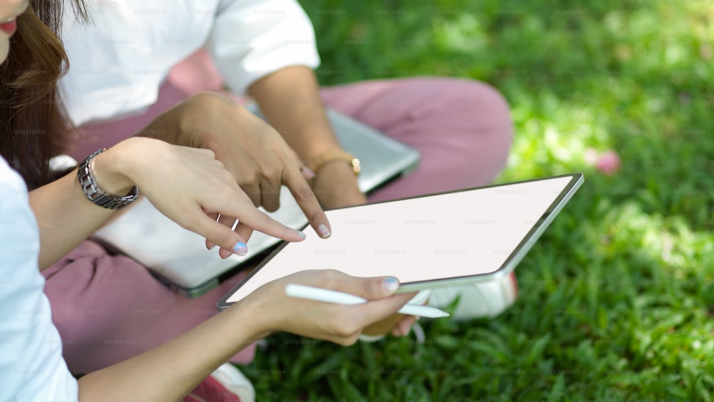 Cropped image of two of female friends sits in a city park looking on digital tablet screen together. working and relaxing concept