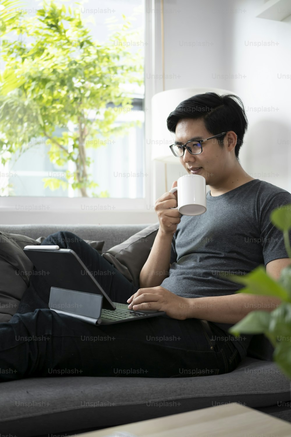 Young man holding coffee cup and working with computer tablet on sofa.