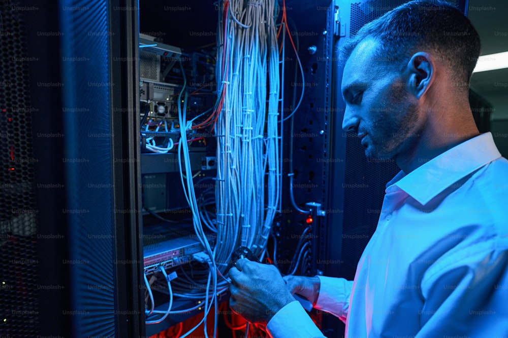 System administrator placing cable connector of twisted pair into crimping tool near server rack