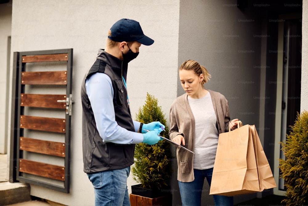 Delivery man with face mask talking to customer who is signing for the package during home delivery.