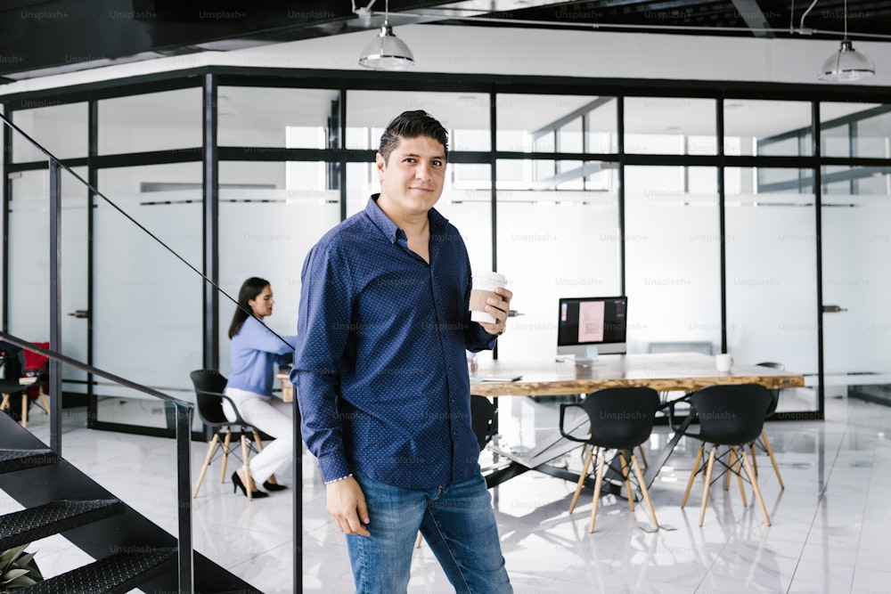 Retrato de un joven oficinista latino con café de pie en la oficina en América Latina