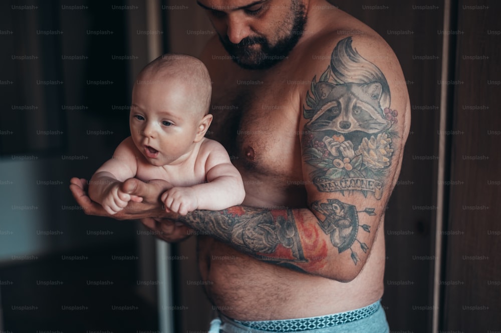 Padre barbuto tatuato che gioca con suo figlio in pannolini mentre è a casa