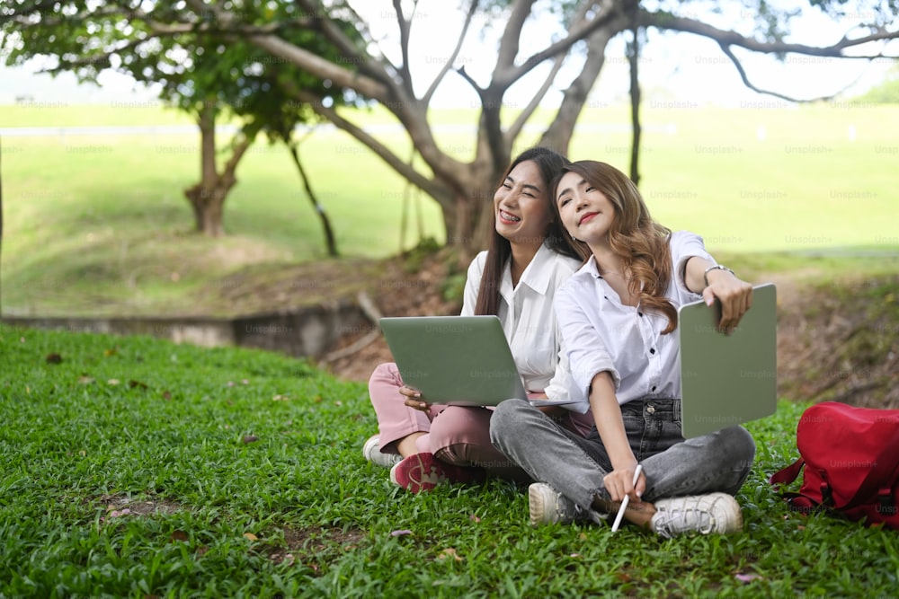 Two university students sitting on grass in the park together.
