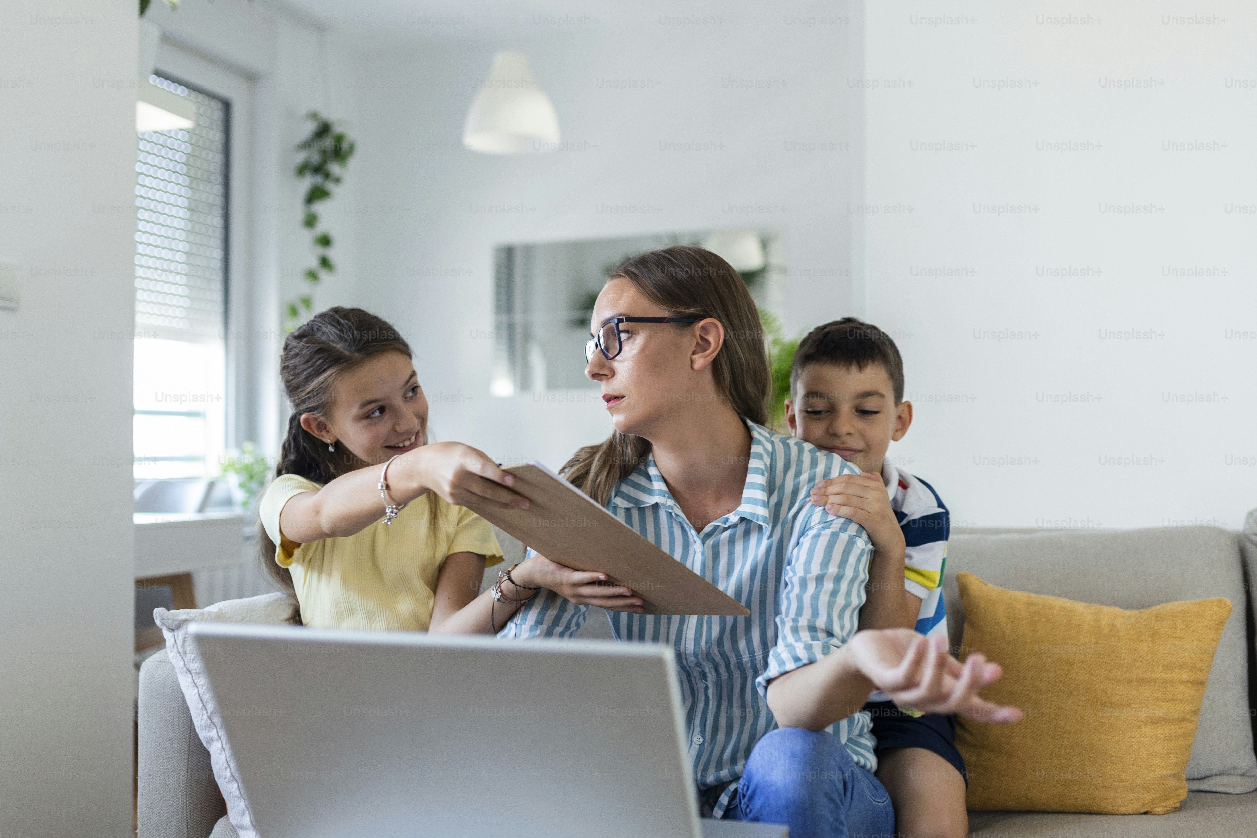 Woman working from home during quarantine with her little son and daughter on couch and screaming, demanding attention